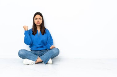 Yerde oturan melez genç kadın mutsuz bir ifadeyle beyaz arka planda izole edilmiş.