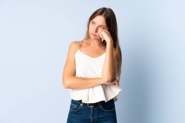 Genç Litvanyalı kadın mavi arka planda izole edilmiş, yorgun ve sıkılmış bir ifadeyle.