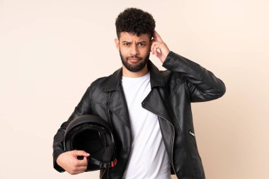 Motosiklet kasklı genç Faslı adam bej arka planda izole edilmiş. Şüpheleri ve düşünceleri var.