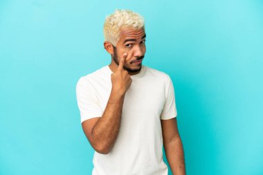 Genç Kolombiyalı yakışıklı adam mavi arka planda izole edilmiş.