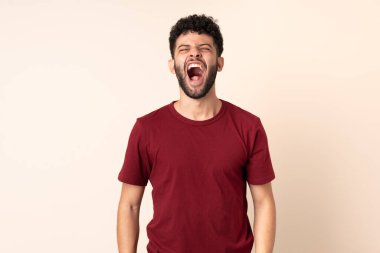 Faslı genç bir adam bej arka planda izole edilmiş ve ağzı açık bağırıyor.