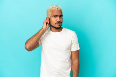 Genç Kolombiyalı yakışıklı adam mavi arka planda izole edilmiş. Şüpheleri var.