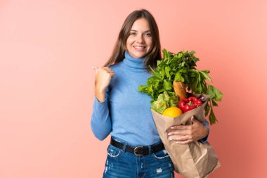 Genç Litvanyalı bir kadın elinde market poşeti ile bir ürün sunmak için kenarı işaret ediyor.