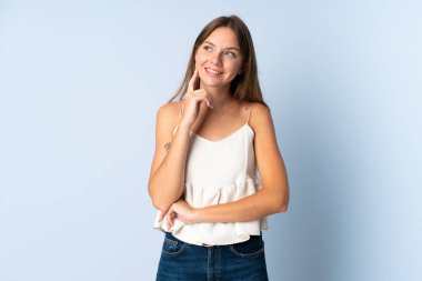 Genç Litvanyalı bir kadın mavi arka planda izole edilmiş, yukarı bakarken bir fikir düşünüyor.