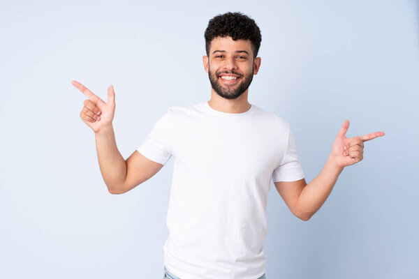 Молодой марокканский человек изолирован на синем фоне указывая пальцем в сторону и счастлив