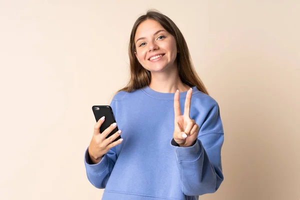 Молода Литовка Користується Мобільним Телефоном Ізольованим Бежевому Фоні Посміхаючись Показуючи — стокове фото