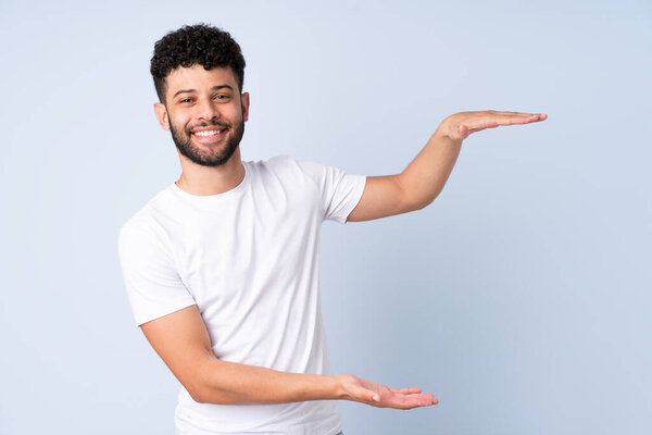 Молодой марокканский человек, изолированный на синем фоне, держит копирайт, чтобы вставить объявление