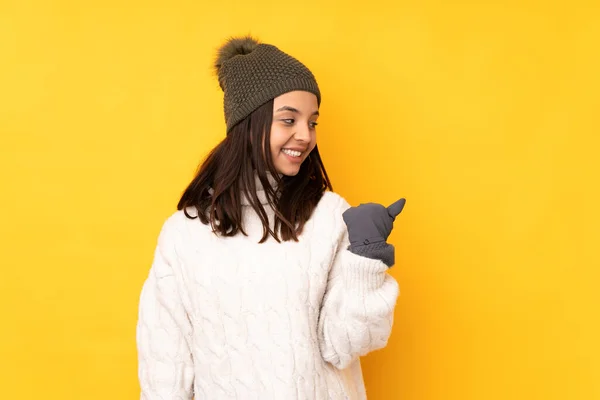 Sarı Arka Planda Kışlık Şapkalı Genç Bir Kadın Bir Ürün — Stok fotoğraf