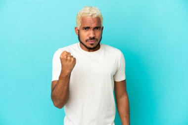 Genç Kolombiyalı yakışıklı adam mutsuz bir ifadeyle mavi arka planda izole edilmiş.