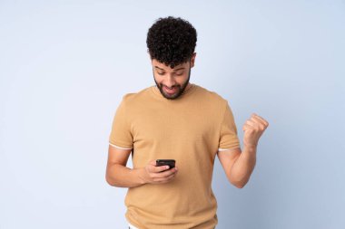 Faslı genç bir adam mavi arka planda izole edilmiş, şaşırmış ve bir mesaj gönderiyor.