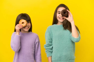Sarı arka planda gözlerinde donut olan küçük kız kardeşler.