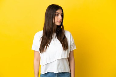 Sarı arka planda izole edilmiş genç beyaz kadın yan tarafa bakıyor.