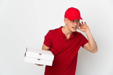 İş üniformalı bir pizzacı beyaz arka planda izole edilmiş pizza kutuları alıyor. Kulağına elini sürerek bir şey dinliyor.