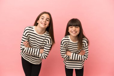 Pembe arka planda izole edilmiş küçük kız kardeşler gülümseyerek kollarını çapraz tutuyorlar.