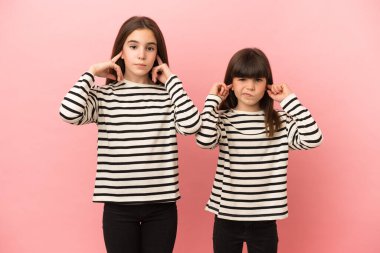 Pembe arka planda izole edilmiş küçük kız kardeşler iki kulağını da elleriyle kapatıyor.