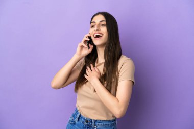 Mor arka planda izole edilmiş cep telefonu kullanan beyaz bir kadın gülümserken yukarı bakıyor.