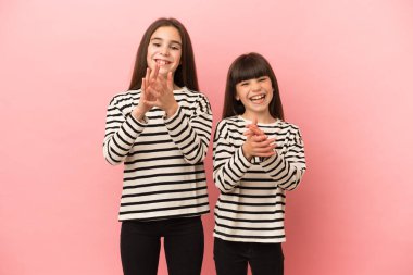 Pembe arka planda izole edilmiş küçük kız kardeşler bir konferansta sunumdan sonra alkışlıyorlar.