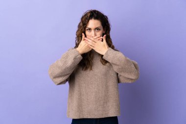 Mor arka planda izole edilmiş genç beyaz kadın elleriyle ağzını kapatıyor.