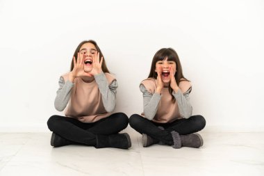 Beyaz arka planda izole bir şekilde yerde oturan küçük kardeşler bağırıyor ve bir şeyler duyuruyorlar.