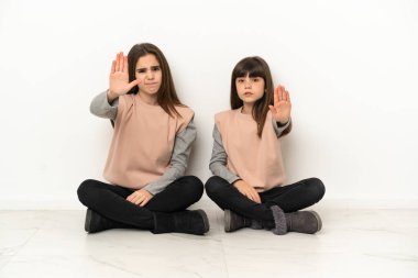 Beyaz arka planda izole bir şekilde yerde oturan küçük kardeşler yanlış bir düşünceyi inkar etmeyi bırakıyorlar.