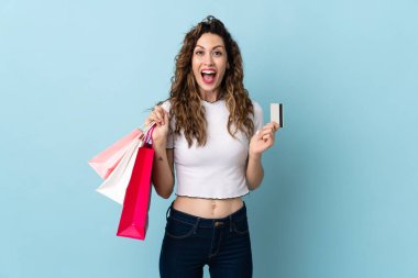 Mavi arka planda izole edilmiş beyaz bir kadın elinde alışveriş torbalarıyla şaşırmış.