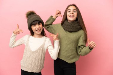 Kışlık kıyafetler giyen küçük kardeşler pembe arka planda soyutlanmış, gururlu ve kendini beğenmiş bir şekilde aşk konseptine sahipler.