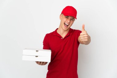İş üniformalı bir pizzacı beyaz arka planda izole edilmiş pizza kutuları alıyor. Başparmakları havada çünkü iyi bir şey oldu.