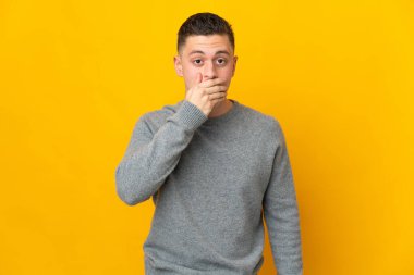 Sarı arka planda izole edilmiş, ağzı elle kaplanmış genç beyaz bir adam.