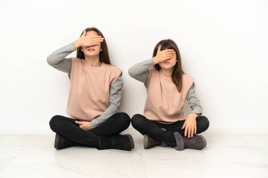 Yerde oturan küçük kız kardeşler, beyaz arka planda tek başlarına, gözleri elleriyle kapatıyorlar. Bir şey görmek istemiyorum.