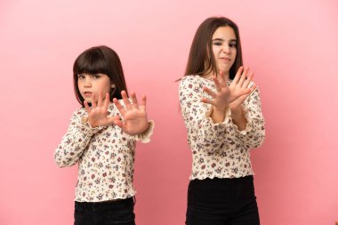 Pembe arka planda izole edilmiş küçük kız kardeşler biraz gergin ve korkmuş bir şekilde ellerini öne uzatıyor.