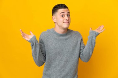 Sarı arka planda izole edilmiş genç beyaz adam şüpheli hareketler yapıyor.