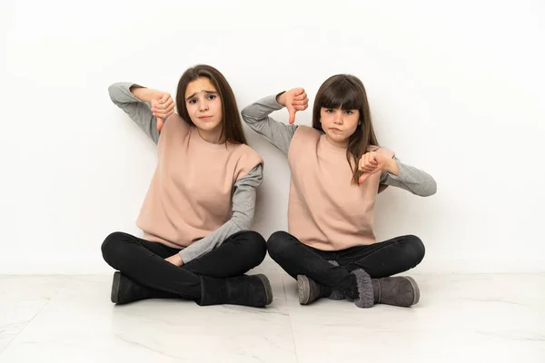 Irmãzinhas Sentadas Chão Isoladas Fundo Branco Mostrando Polegar Para Baixo — Fotografia de Stock