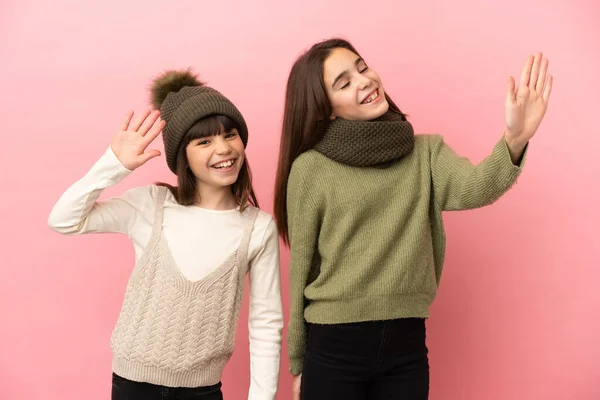 Hermanitas Vestidas Con Ropa Invierno Aisladas Sobre Fondo Rosa Saludando —  Fotos de Stock