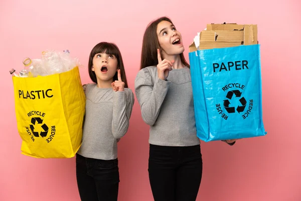 Irmãzinhas Reciclando Papel Plástico Isolado Fundo Rosa Pensando Uma Ideia — Fotografia de Stock