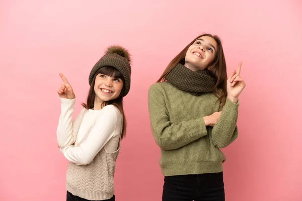 Irmãzinhas Vestindo Uma Roupa Inverno Isolada Fundo Rosa Apontando Uma — Fotografia de Stock