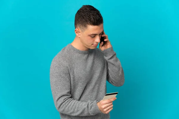 Young caucasian man isolated on blue background buying with the mobile with a credit card