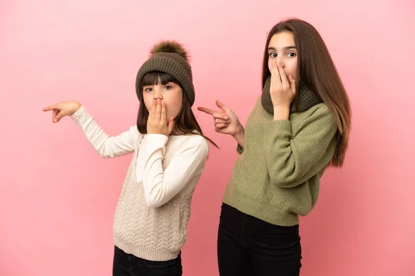 Små Systrar Bär Vinter Kläder Isolerad Rosa Bakgrund Pekar Finger — Stockfoto