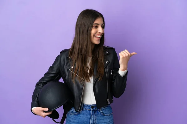 若いですCaucasian女性でオートバイのヘルメットは 製品を提示する側を指して紫色の背景に隔離されました — ストック写真