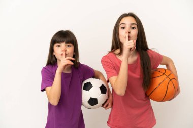 Beyaz arka planda izole edilmiş futbol ve basketbol oynayan küçük kız kardeşler parmaklarını ağzına koyan sessiz bir jest işareti gösteriyorlar.