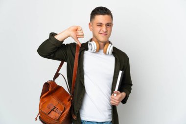 Beyaz arka planda izole edilmiş beyaz tenli genç bir öğrenci negatif ifadeyle baş parmağını aşağı gösteriyor.