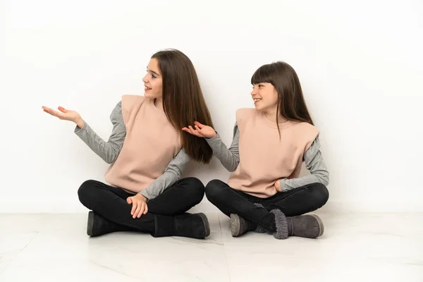 Маленькі Сестри Сидять Підлозі Ізольовані Білому Тлі Вказуючи Назад Представляючи — стокове фото