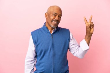 Kübalı son sınıf öğrencisi pembe arka planda izole edilmiş gülümsüyor ve zafer işareti gösteriyor