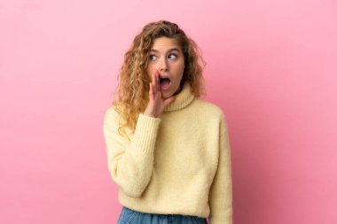 Pembe arka planda soyutlanmış genç sarışın kadın yan tarafa bakarken sürpriz bir jest yapıyor.