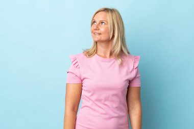 Mavi arka planda soyutlanmış orta yaşlı bir kadın yan bakıyor ve gülümsüyor.