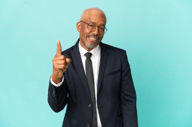 İşletme son sınıf öğrencisi mavi arka planda izole edilmiş ve en iyinin işareti olarak parmağını kaldırıyor.