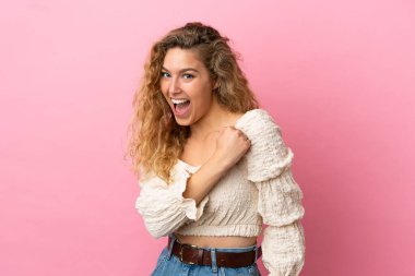 Pembe arka planda izole edilmiş genç sarışın kadın zaferi kutluyor.