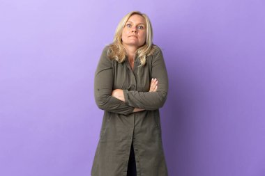 Orta yaşlı Litvanyalı kadın mor arka planda izole edilmiş. Omuzlarını kaldırırken şüpheyle hareket ediyor.