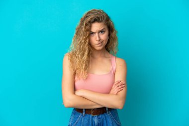 Genç sarışın kadın mutsuz bir ifadeyle mavi arka planda izole edilmiş.