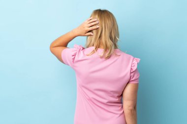 Orta yaşlı bir kadın mavi arka planda izole edilmiş ve düşünüyor.