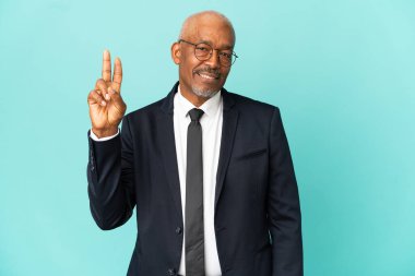 İşletme son sınıf öğrencisi mavi arka planda izole edilmiş gülümsüyor ve zafer işareti gösteriyor.